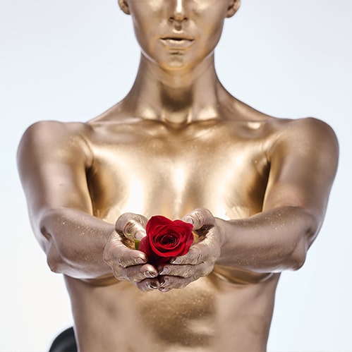 woman covered with gold paint holding rose in her hands