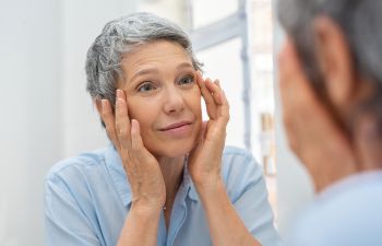 Senior woman checking her skin around eyes in the mirror.
